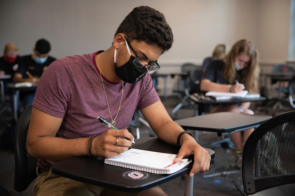 masked student writing in notebook