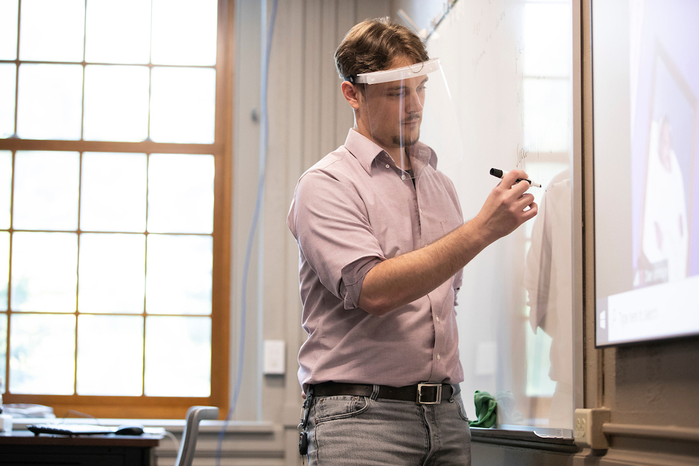 Male teacher with a transparent face shield write on whiteboard