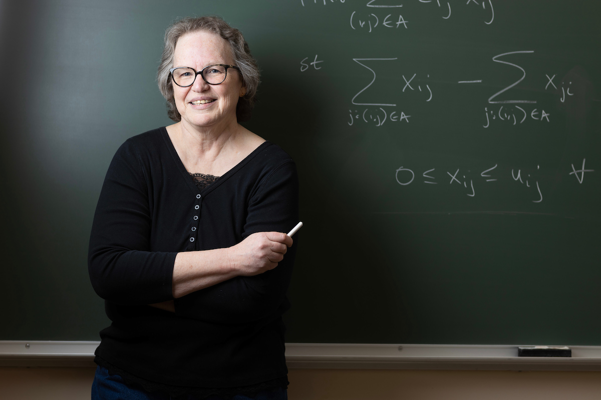 Dr. Betty Love smiles in front of a chalkboard on which she has written a few math equations.