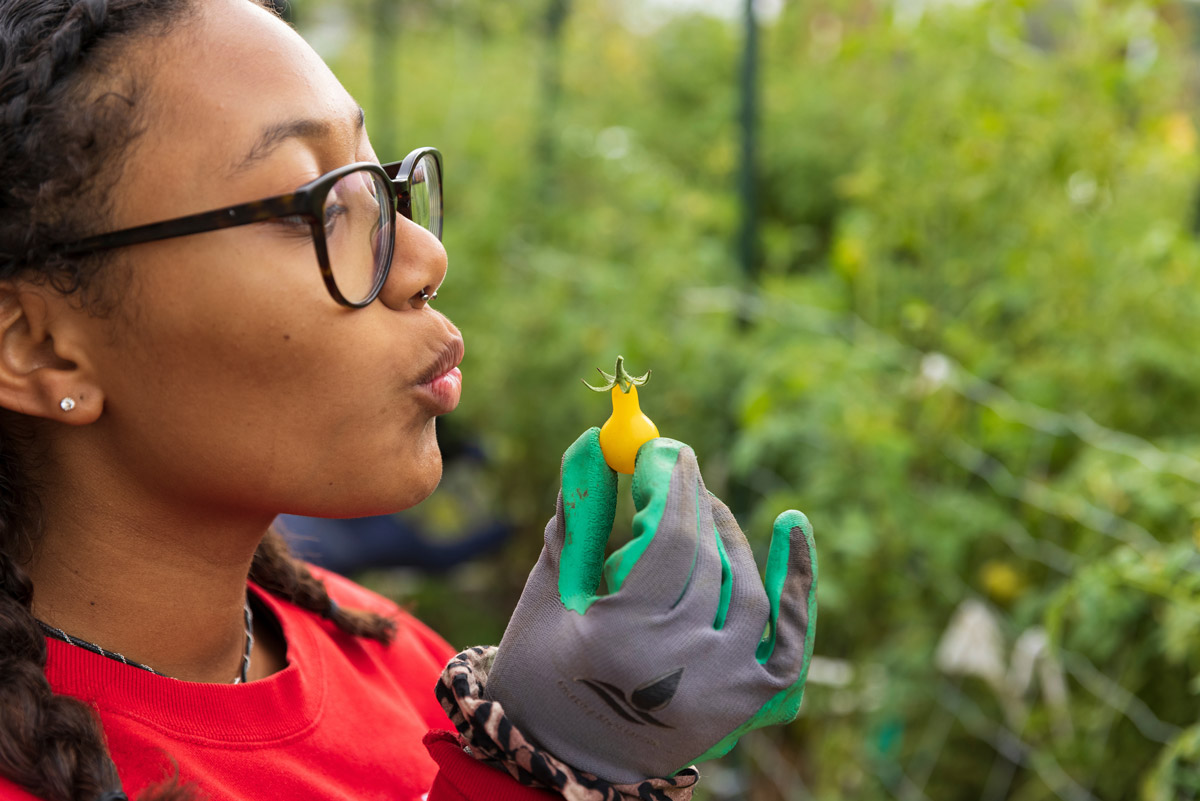 A woman blows a kiss to a small yellow tomato held in her hand.