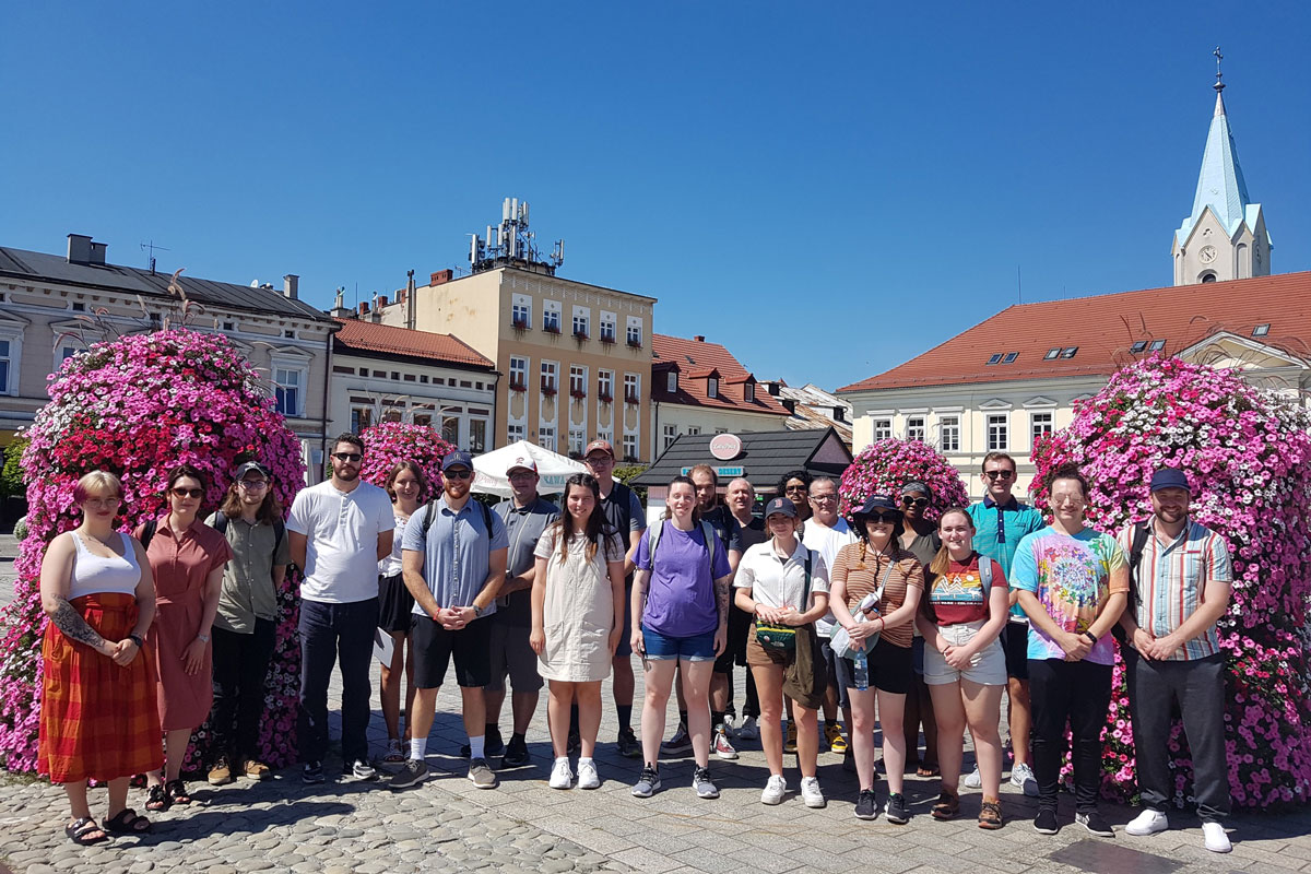 A group photo of students standing in a square outside and surrounded by pink flowers.