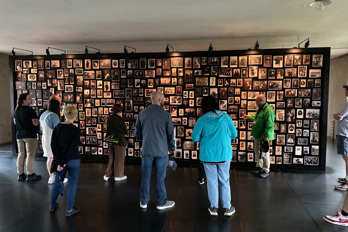 People stand and look at a wall of photos as part of an Auschwitz Memorial exhibit.