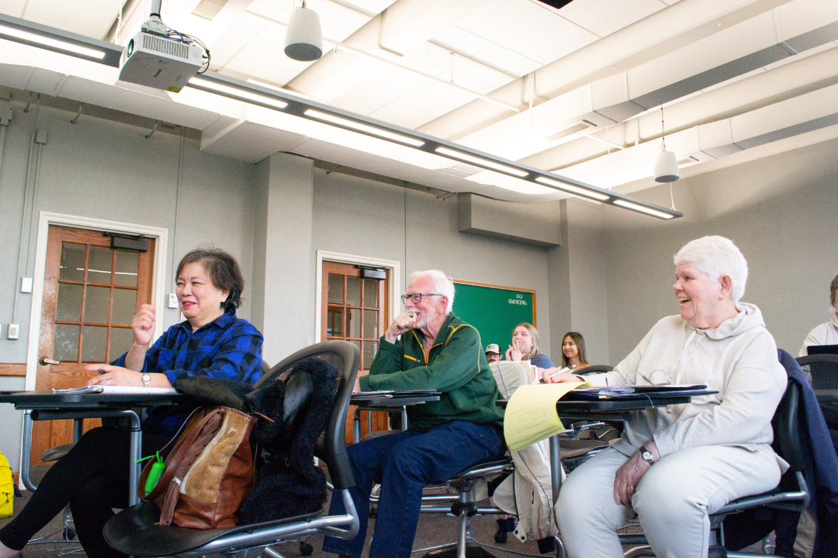 Three students sit together and smile in a classroom.