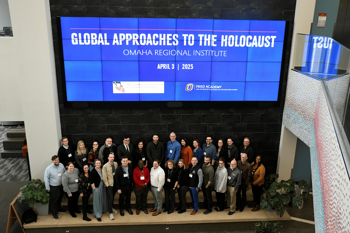 Attendees stand in front of a blue sign that says "Global Approaches to the Holocaust."