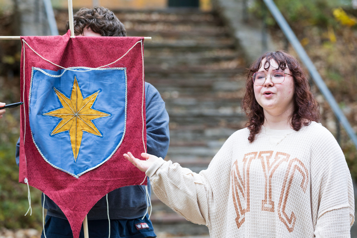 Izzy Martin stands next to a medieval flag. 