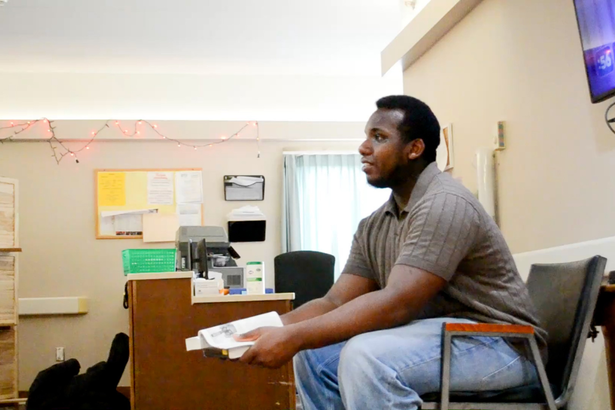 Kiere sits at a chair holding a book.