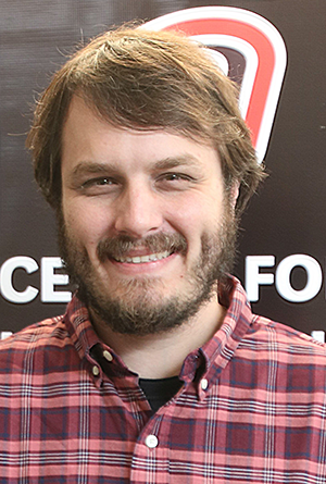 Dr. William Kramer is wearing a red plaid shirt and has brown hair and a beard.