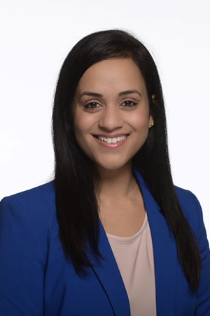 Dr. Mahima Saxena has long dark hair and is wearing a bright blue jacket.