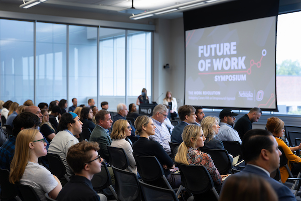 Panelists discuss the future of work on stage while an audience listens.