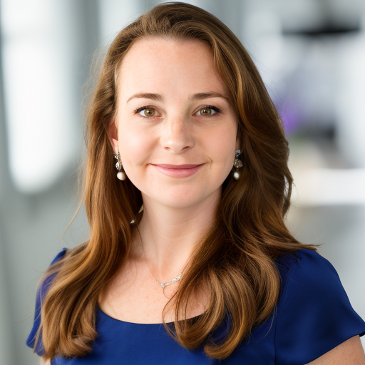 Professional headshot of a person with long brown hair wearing a royal blue blouse, pearl drop earrings, and a delicate necklace. They are smiling gently at the camera against a softly blurred office-style background in neutral tones.
