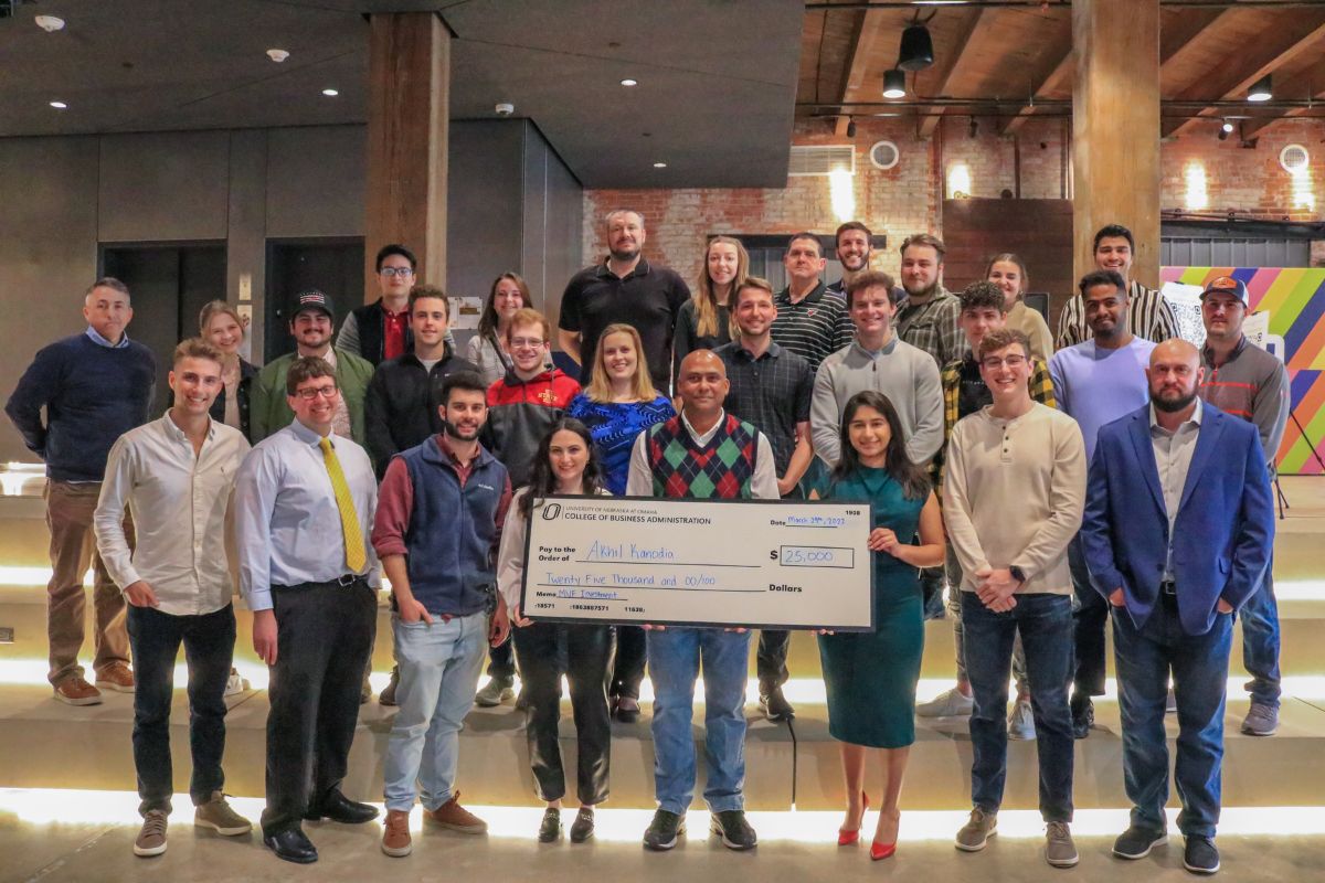 An image of people surrounding a man in the center holding a giant check