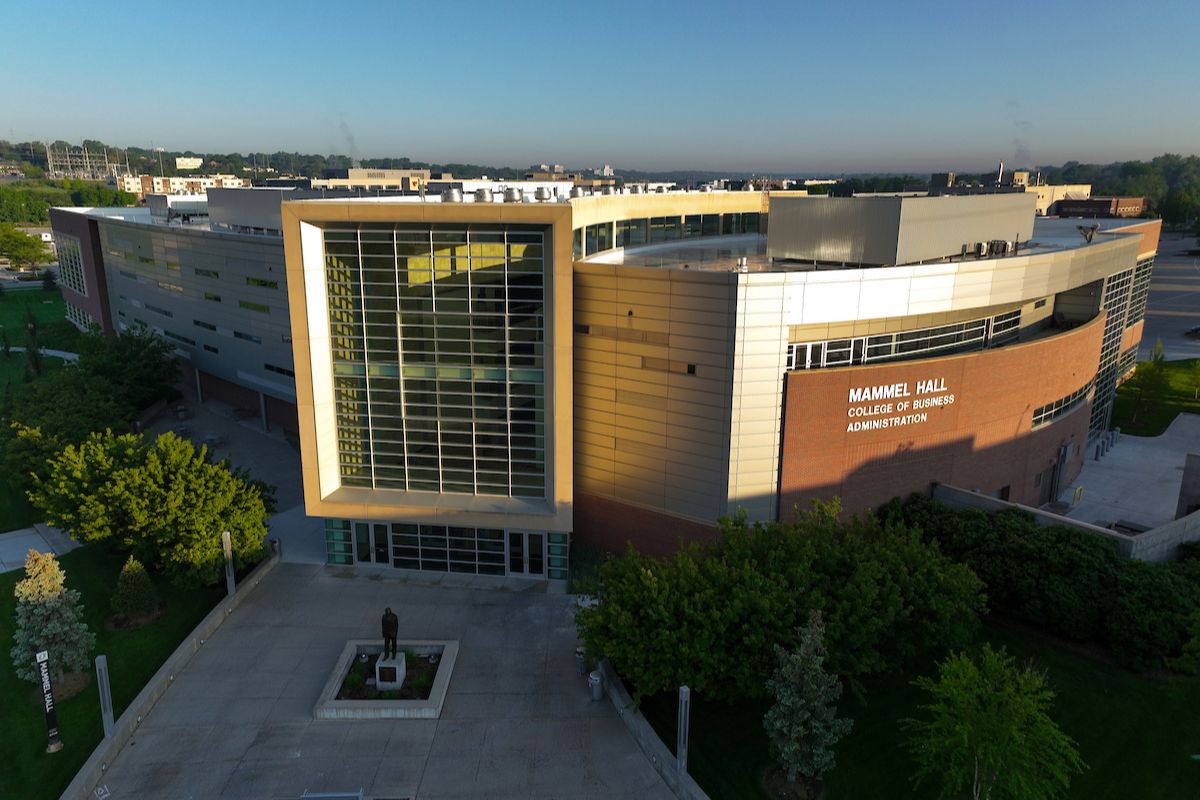 A drone image of a large college building with glass windows. The sun shines on the building.