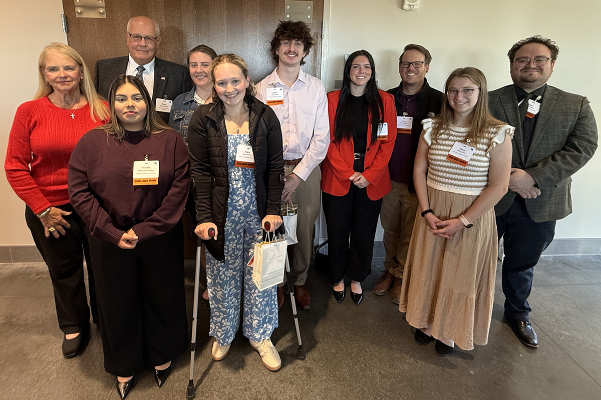 A group of ten people pose together indoors, smiling for a photo. They are wearing business or business-casual clothing and name tags, standing in front of a wooden door in a well-lit room.