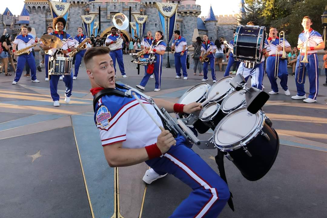 Fay Porter making an enthusiastic expression while playing the drums in marching band uniform at Disneyland