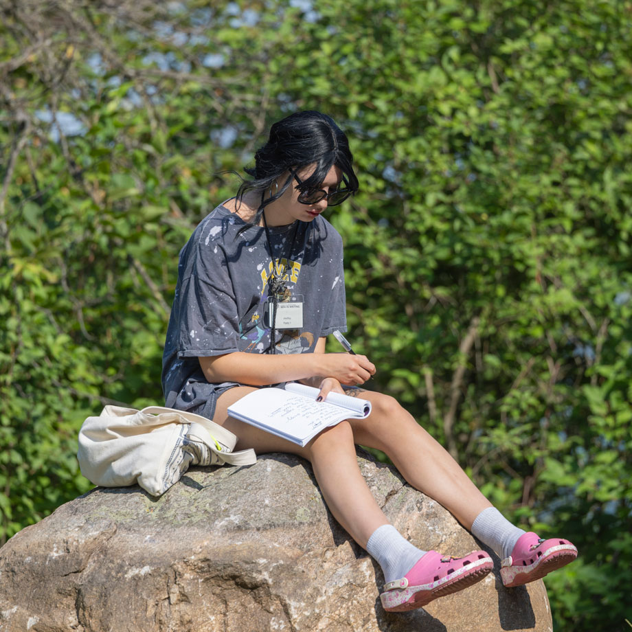 Student sitting on rock while writing. 