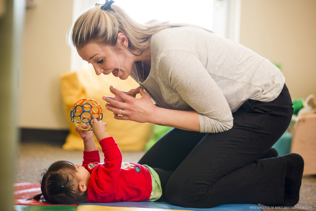 A childcare teacher actively plays with a toddler using a colorful ball