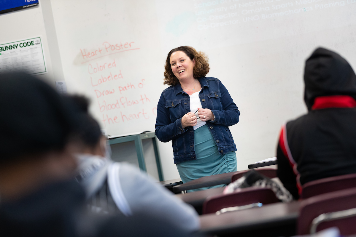 A teacher stands at the front of a classroom, smiling at her students