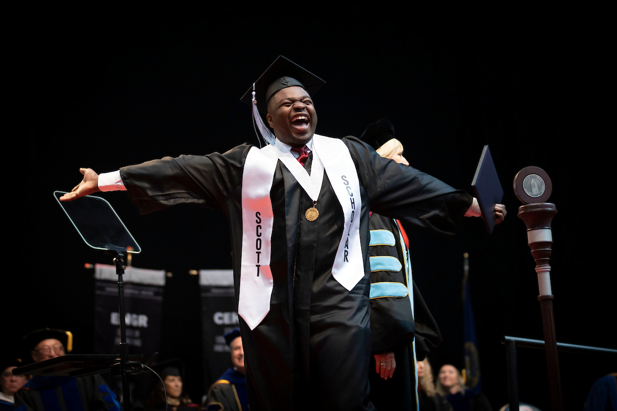 person wearing cap and gown celebrates graduating with arms extended and smile.