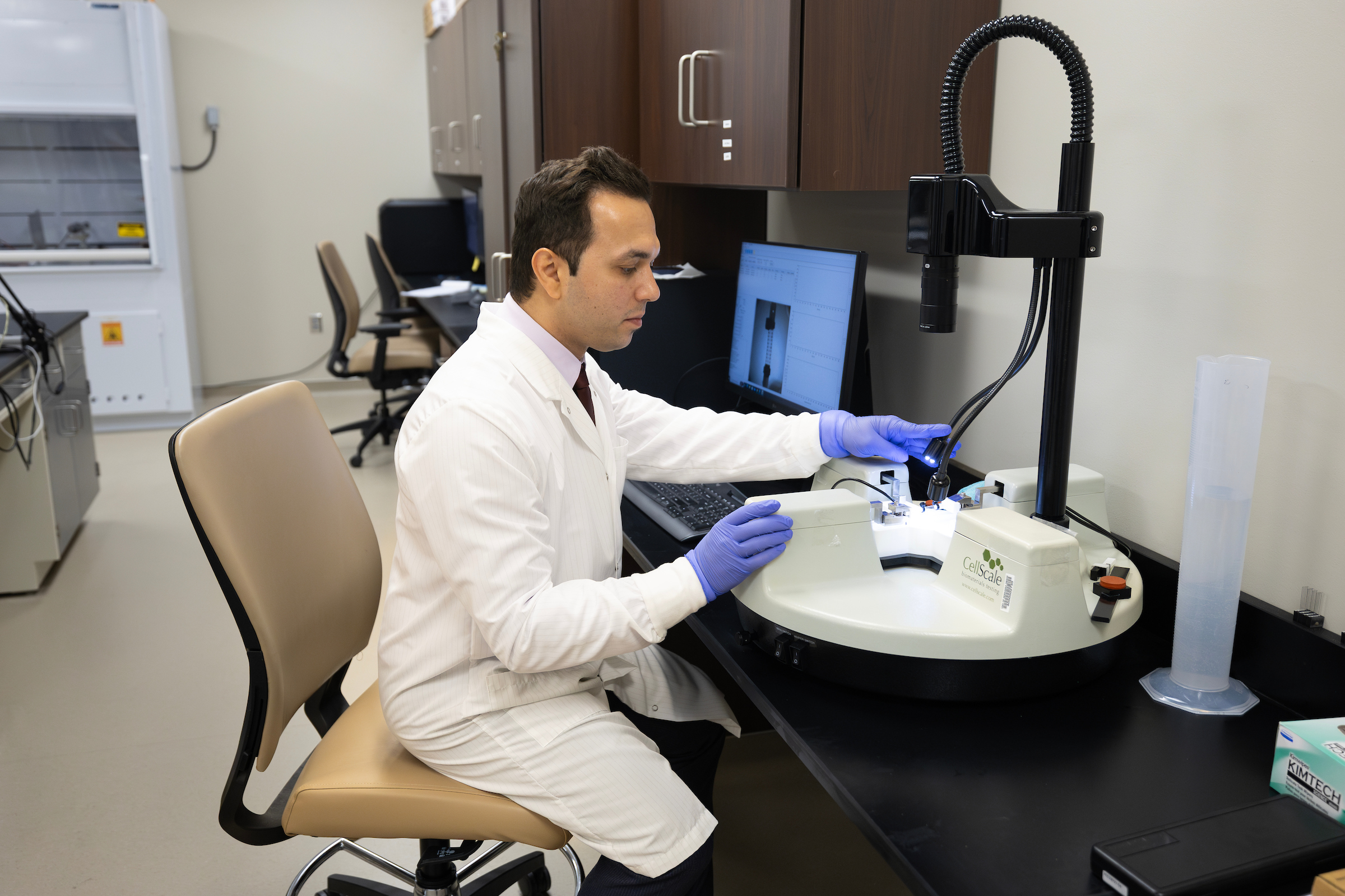 man in lab coat and gloves operates lab equipment in a wet lab.