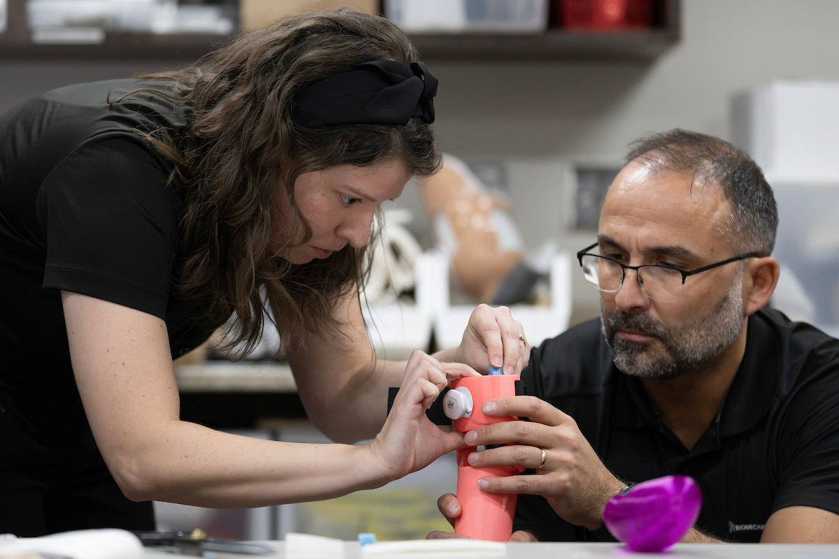 two people work together on a pink 3d printed prosthetic arm for a child