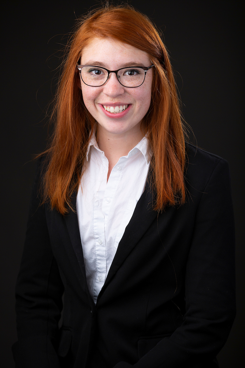 a person with long red hair wearing glasses and a button up white shirt with a suit jacket.
