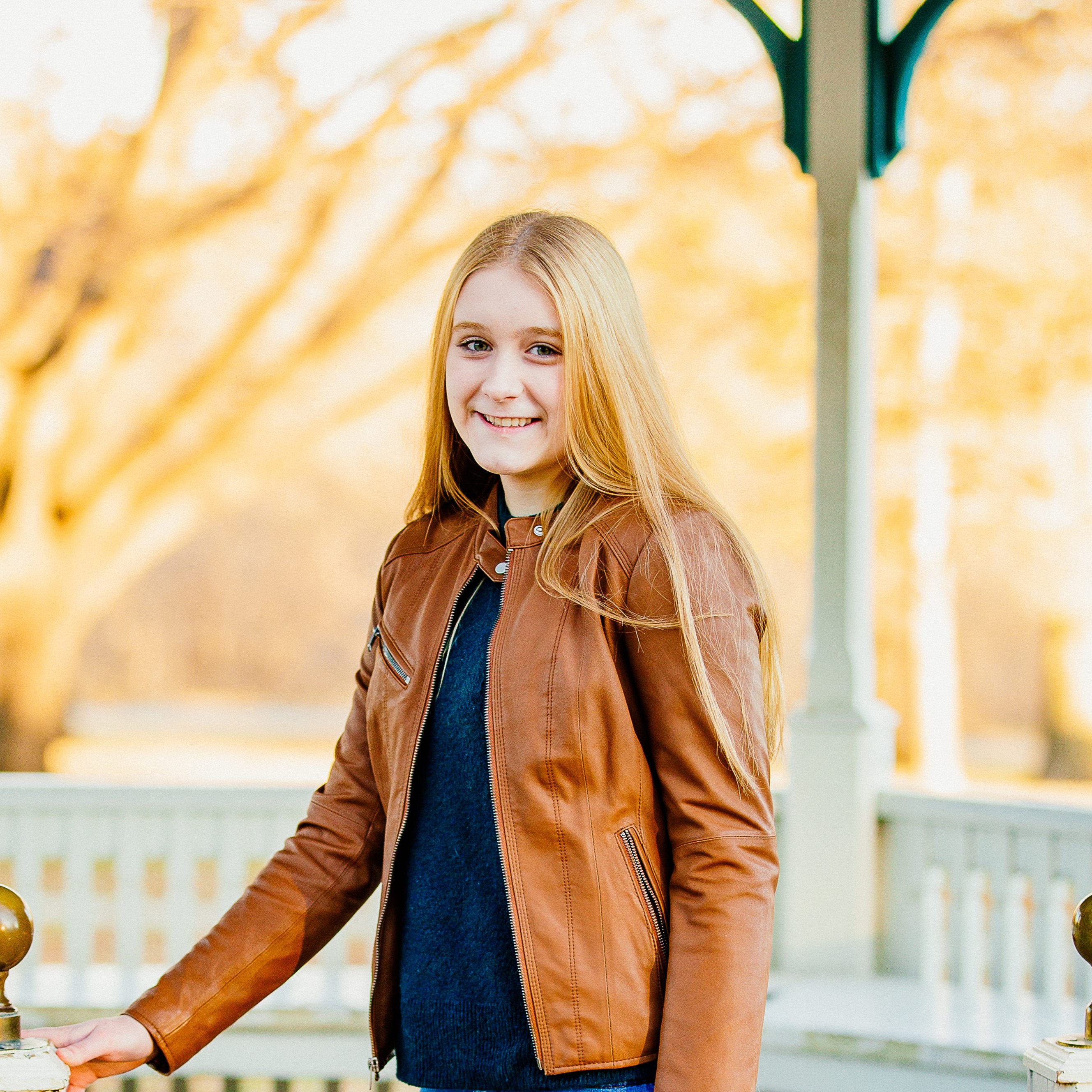 a person with long blonde hair smiling while standing on a white porch.