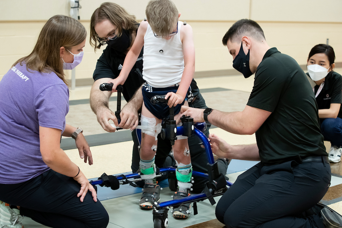 clinicians help a young boy with cerebral palsey use a specially designed walker