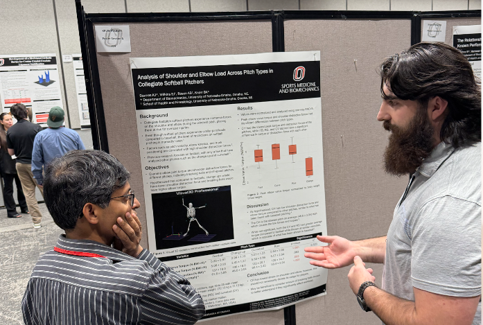 An individual presenting a scientific research poster to an individual at the Great Plains Biomechanics conference.