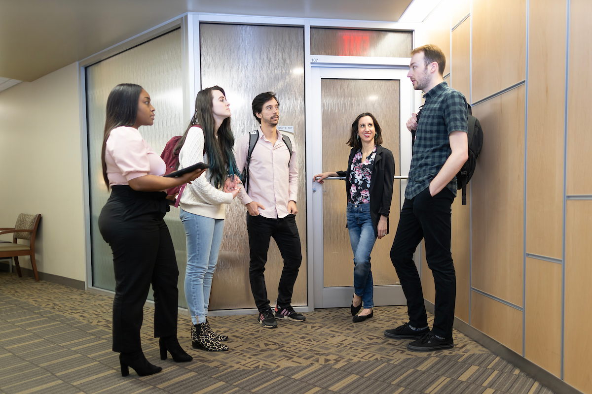 A group of students stand in front of UNO's Community Counseling Clinic, talking in a casual manner