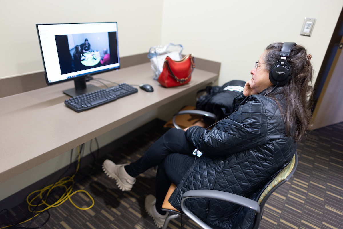 A person wears headphones and observes a session in the Speech-Language Clinic on a computer