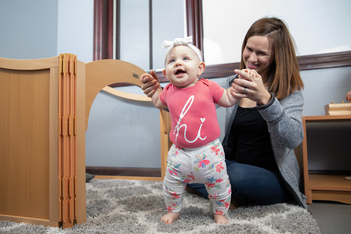 A woman helps a baby stand in a playroom