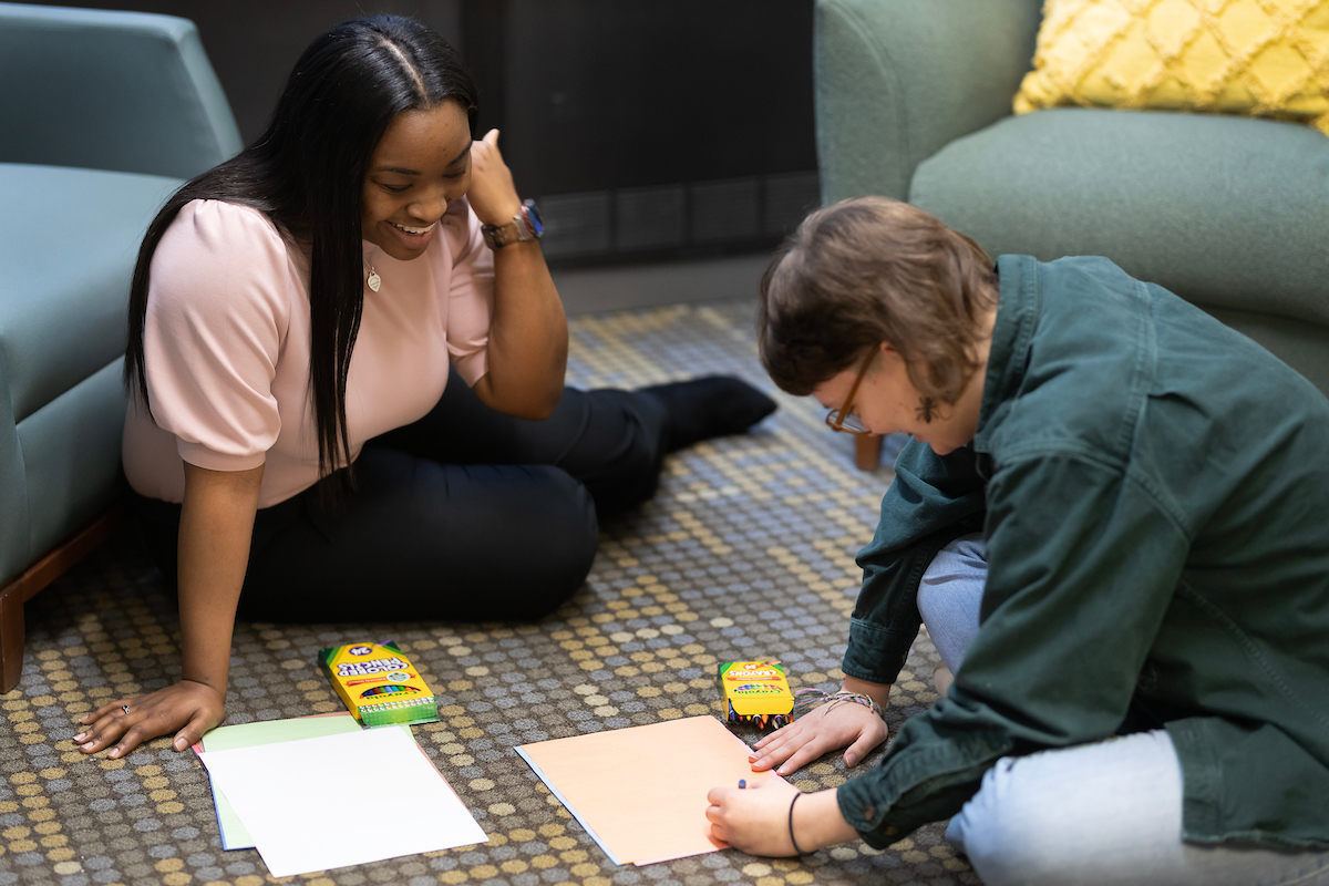 A grad student and a client sit on the floor of a counseling room during an art therapy session