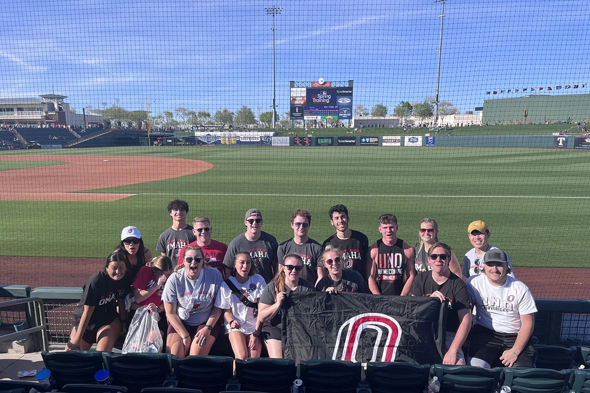 A group of people hold a UNO flag in a baseball stadium.