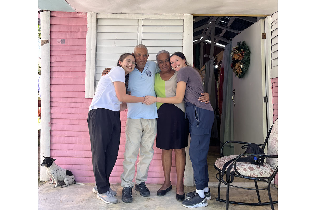 Four people hug on the front porch of a small pink house