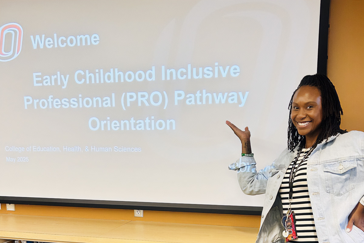 A woman holds her hand up to a presentation screen and smiles
