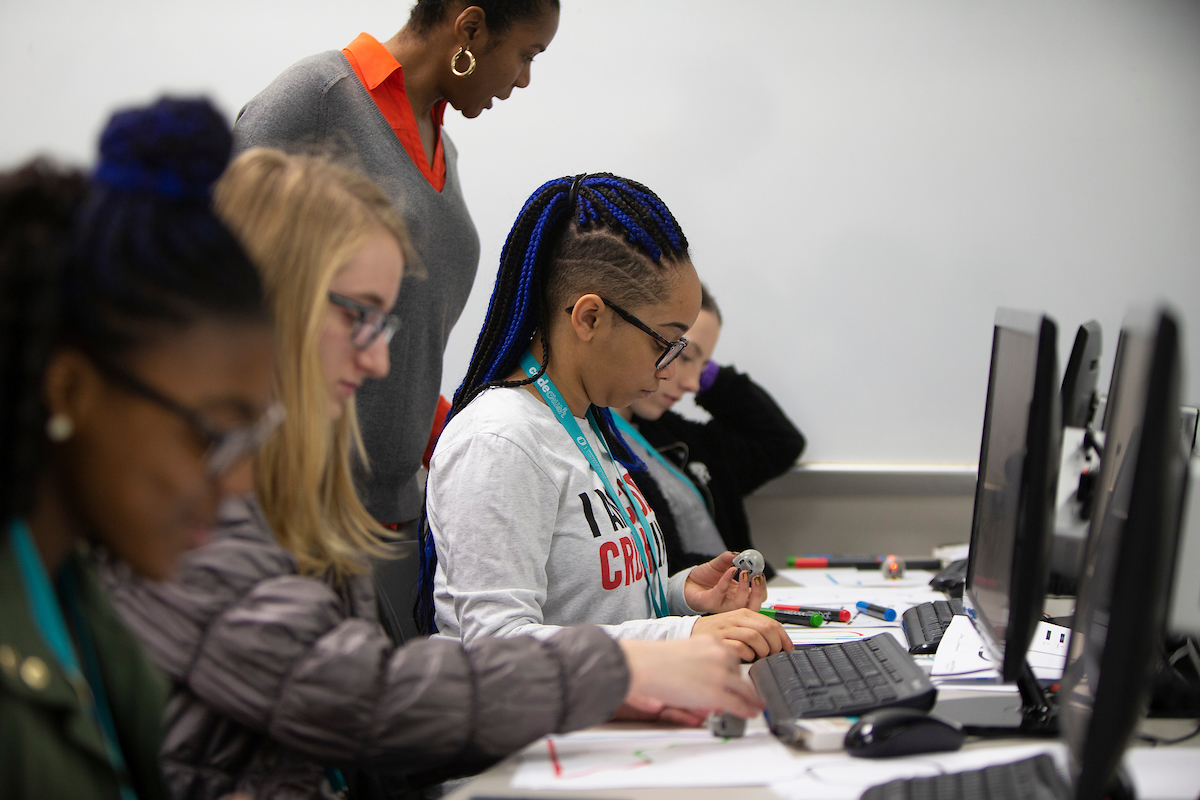 Students work on computers with a teacher looking on