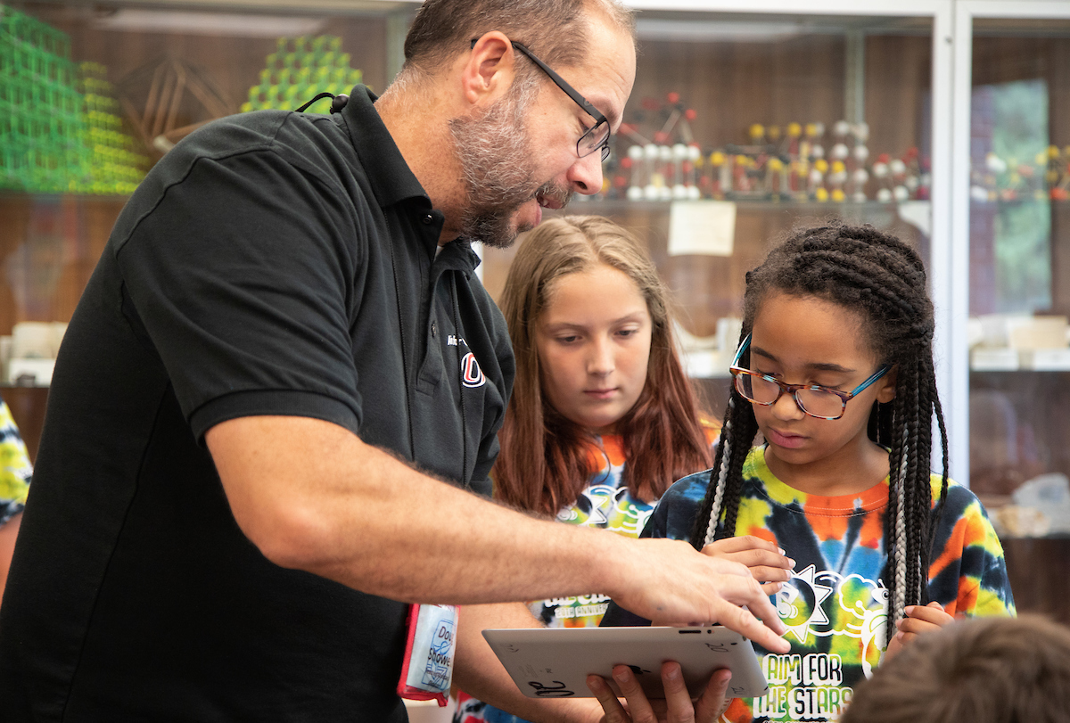 A teacher holding an iPad demonstrates to two children