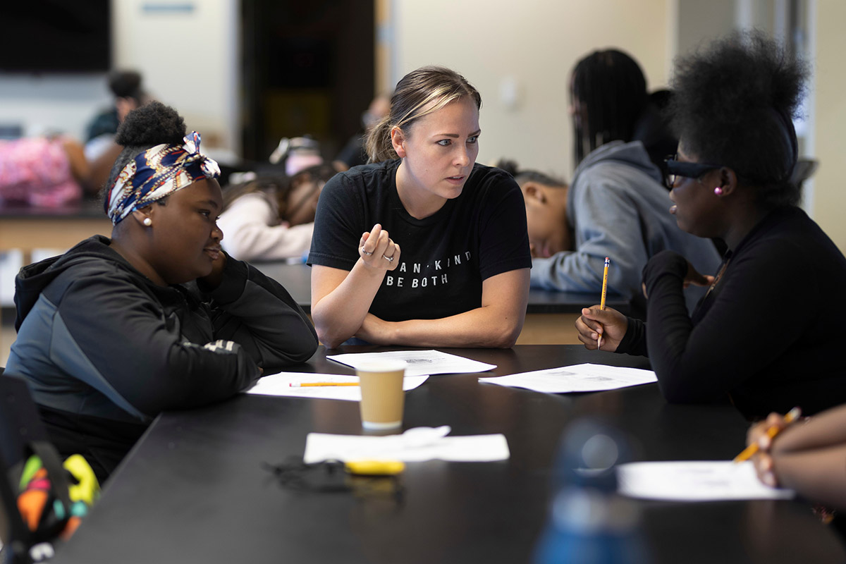 A teacher helps two teenage student in a classroom