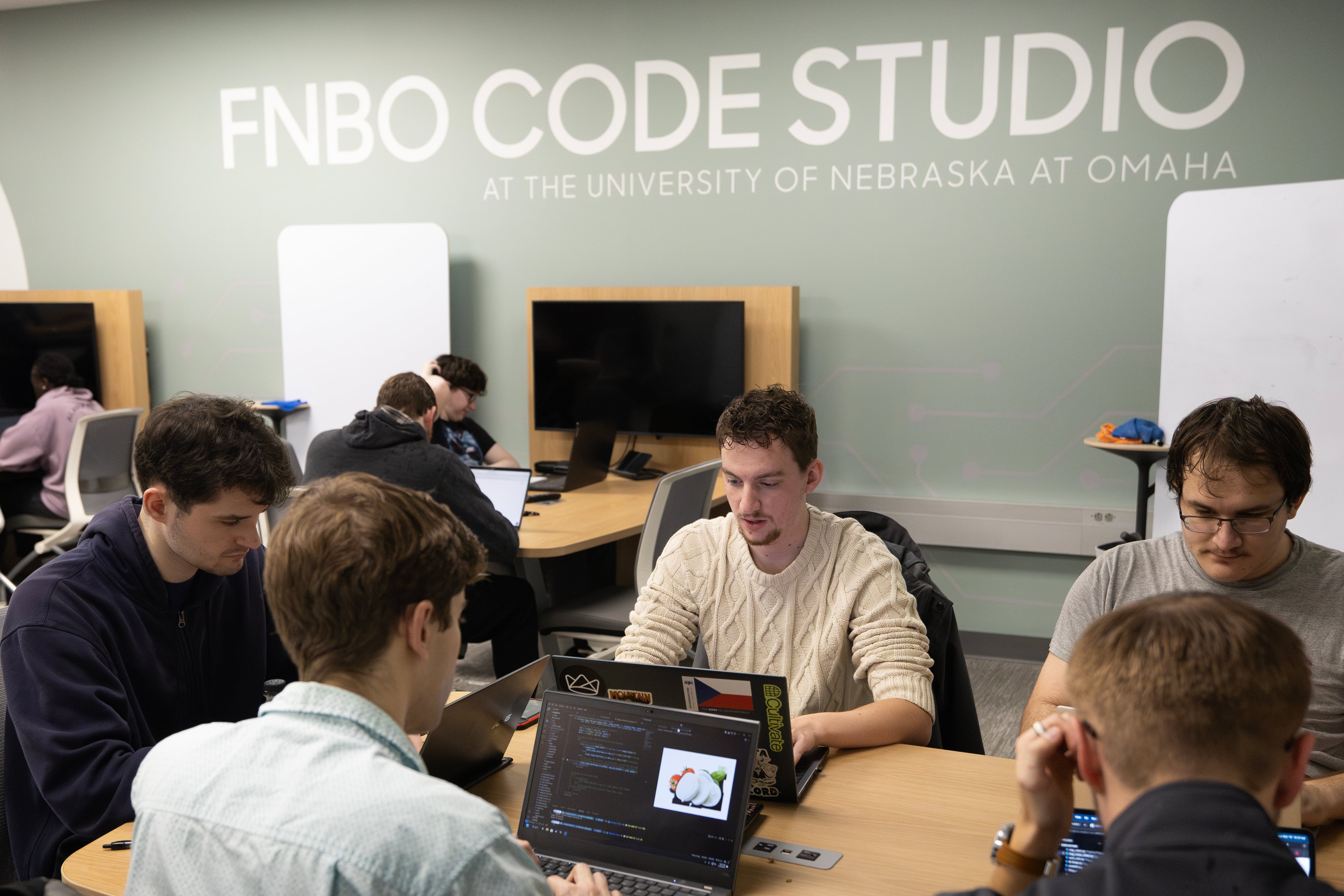 Students collaborating on laptops at tables in FNBO Code Studio