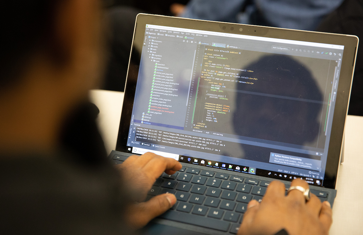 Student coding on a laptop with a code editor and terminal window visible on screen during a capstone project session.