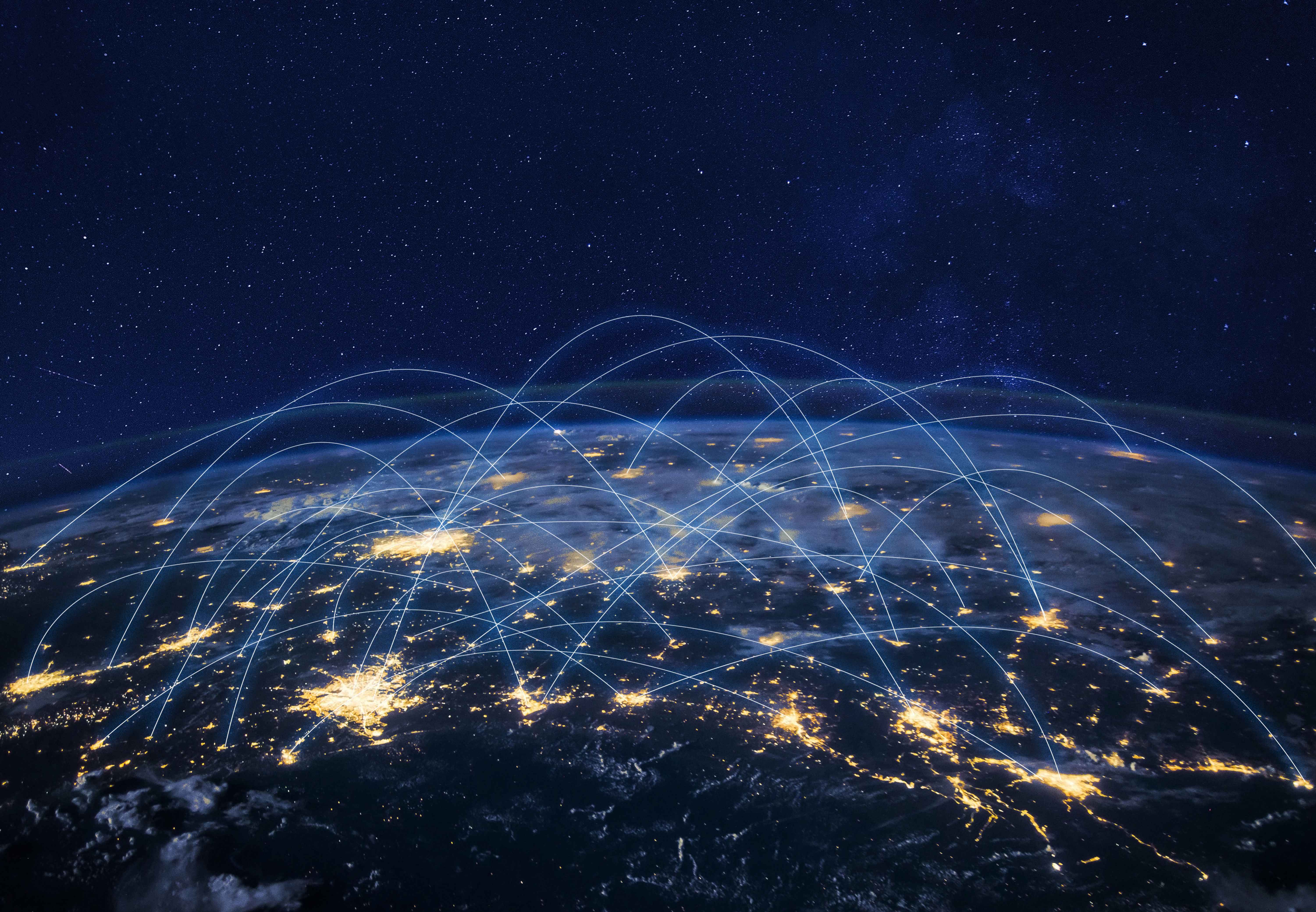 View of Earth from space at night with glowing blue arcs connecting continents, symbolizing worldwide digital networks and data transfer.