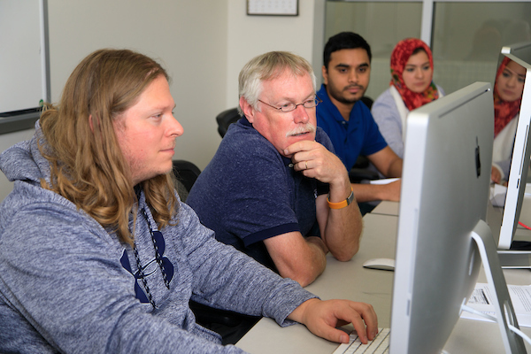 Two males, one a student and one a professor, work at a computer.