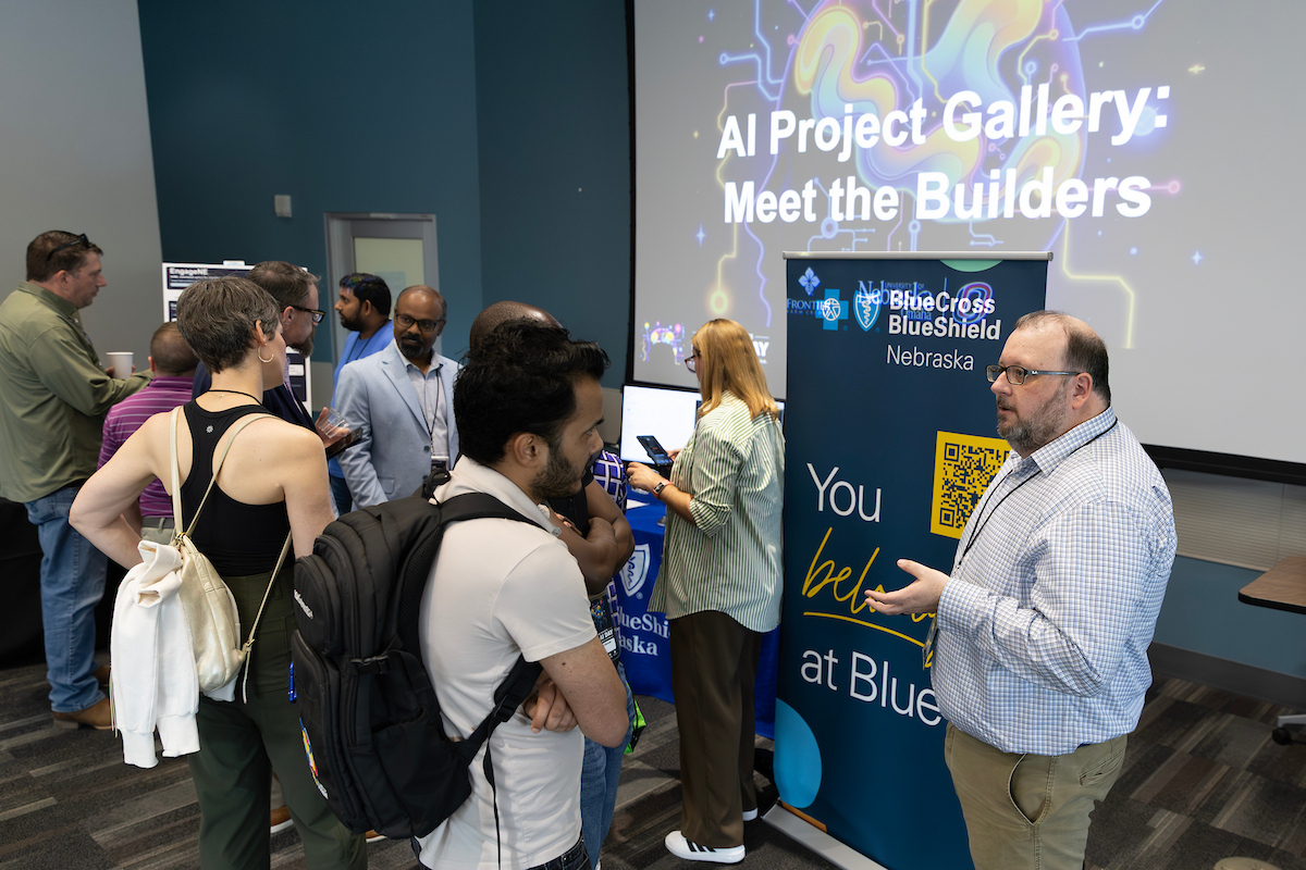 This image shows a woman talking to a student in the foreground during a technology career fair event.