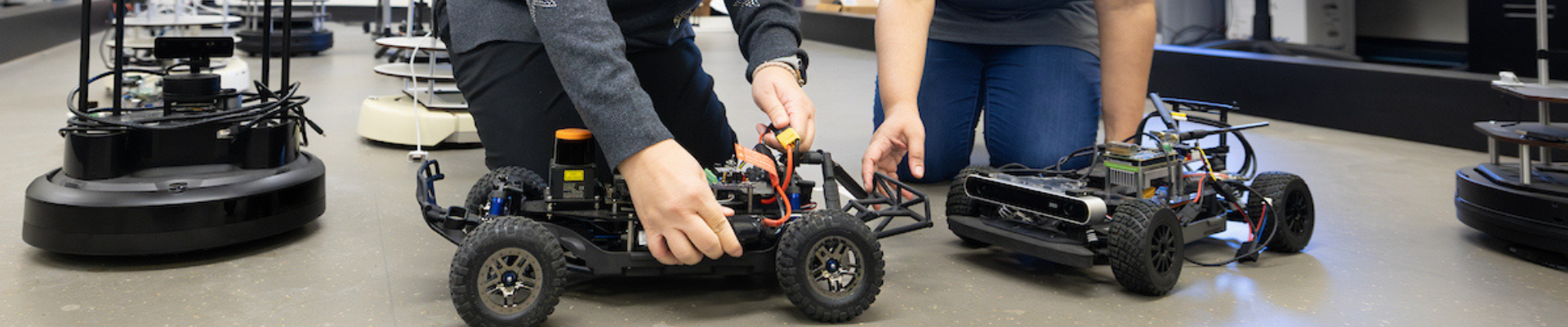 Two students assemble robotic vehicles in a robotics lab.