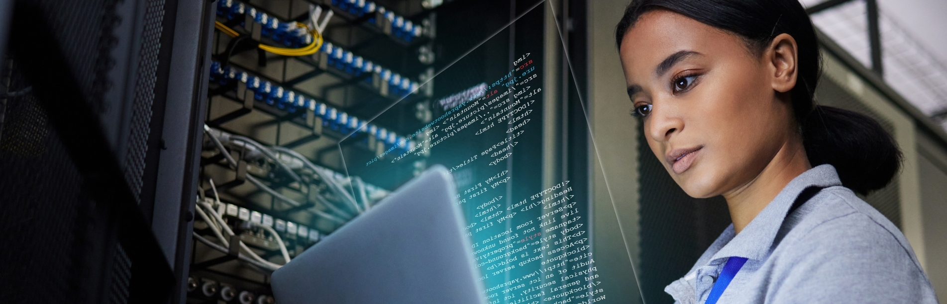 A person sits in front of an open laptop in a server room, surrounded by racks filled with cables and hardware.