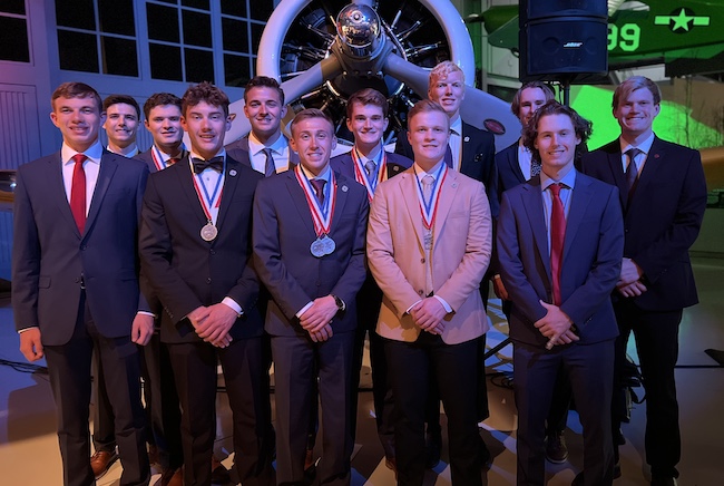 flight team competitors in front of plane with awards and medals