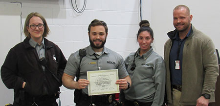 Four people in a row. One is holding a certificate. 