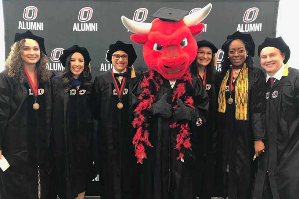 2018 doctoral program graduates in caps and gown, with Durango, the UNO mascot.