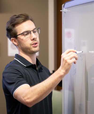 Instructor writing on a white board in front of a classroom.