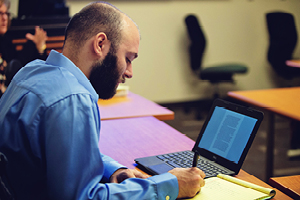 Man writing in notebook with laptop open next to him.